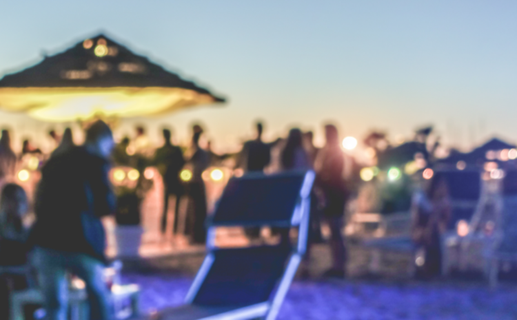 featured image blury photo of an outside beach party where people are not practicing social distancing