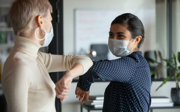 FEatured image showing diverse female colleagues wearing protective face masks greeting bumping elbows at workplace