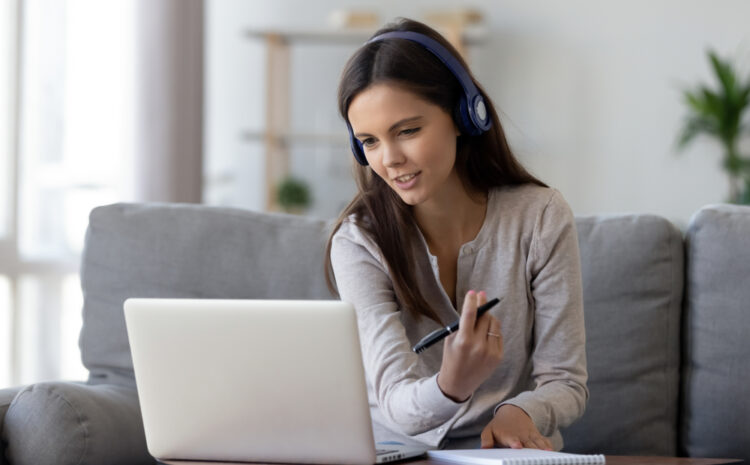 featured image showing a Happy young woman in headphones speaking looking at laptop making notes