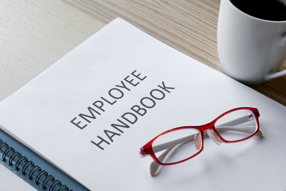 Featured image showing an employee handbook on a desk with glasses